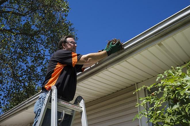 a roofer repairing a damaged gutter on a house in Carol Stream